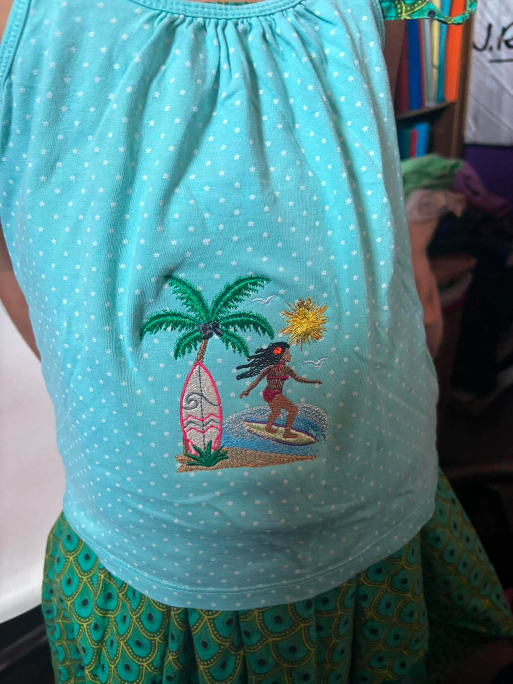 Motif de broderie Surfeuse disponible au format 10x10. Décor tropical avec palmier, planche de surf, océan et soleil, idéal pour une ambiance estivale.