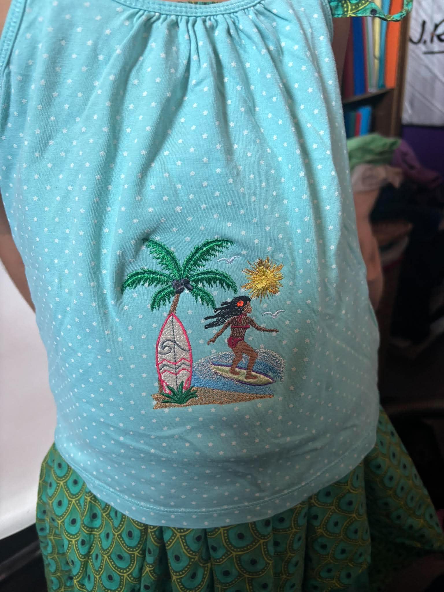 Motif de broderie Surfeuse disponible au format 10x10. Décor tropical avec palmier, planche de surf, océan et soleil, idéal pour une ambiance estivale.