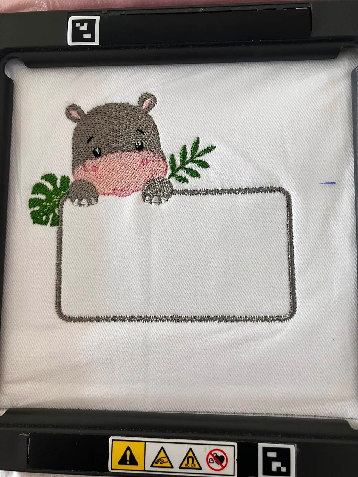 Motif de broderie Étiquette Hippopotame personnalisable avec feuillages et cadre pour ajouter un prénom ou un texte au format 10x10