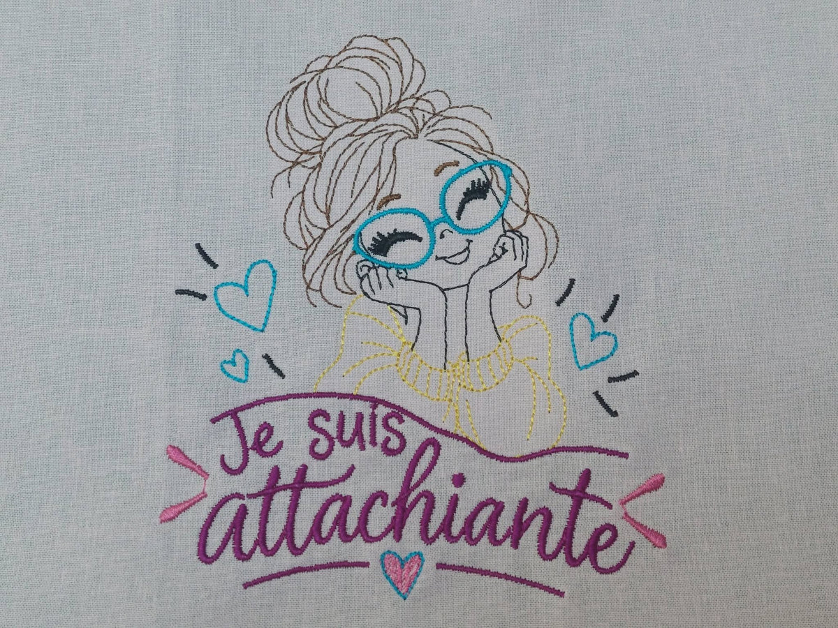 Je suis Attachiante – femme avec chignon, grandes lunettes rouges et petits cœurs – motif de broderie machine humour