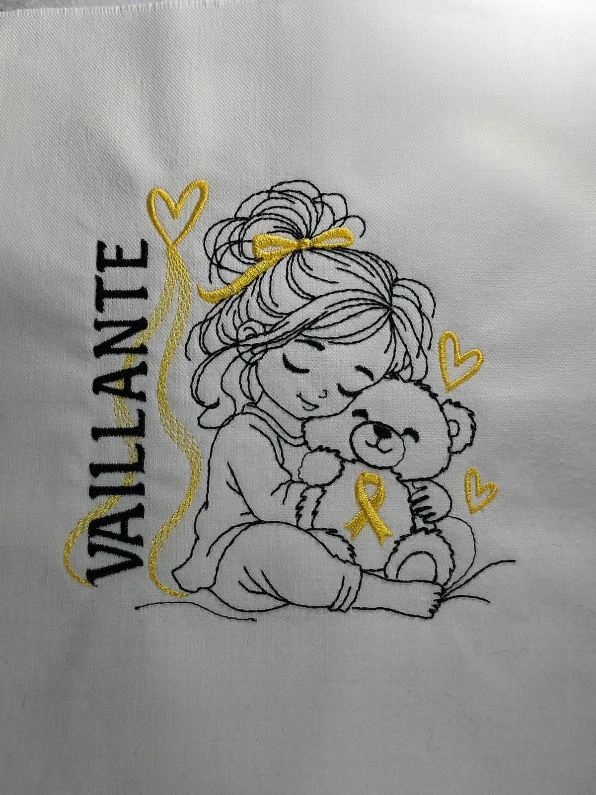 La Petite Vaillante, petite fille serrant un ourson avec ruban doré, cœurs et message VAILLANTE – motif broderie Septembre en Or