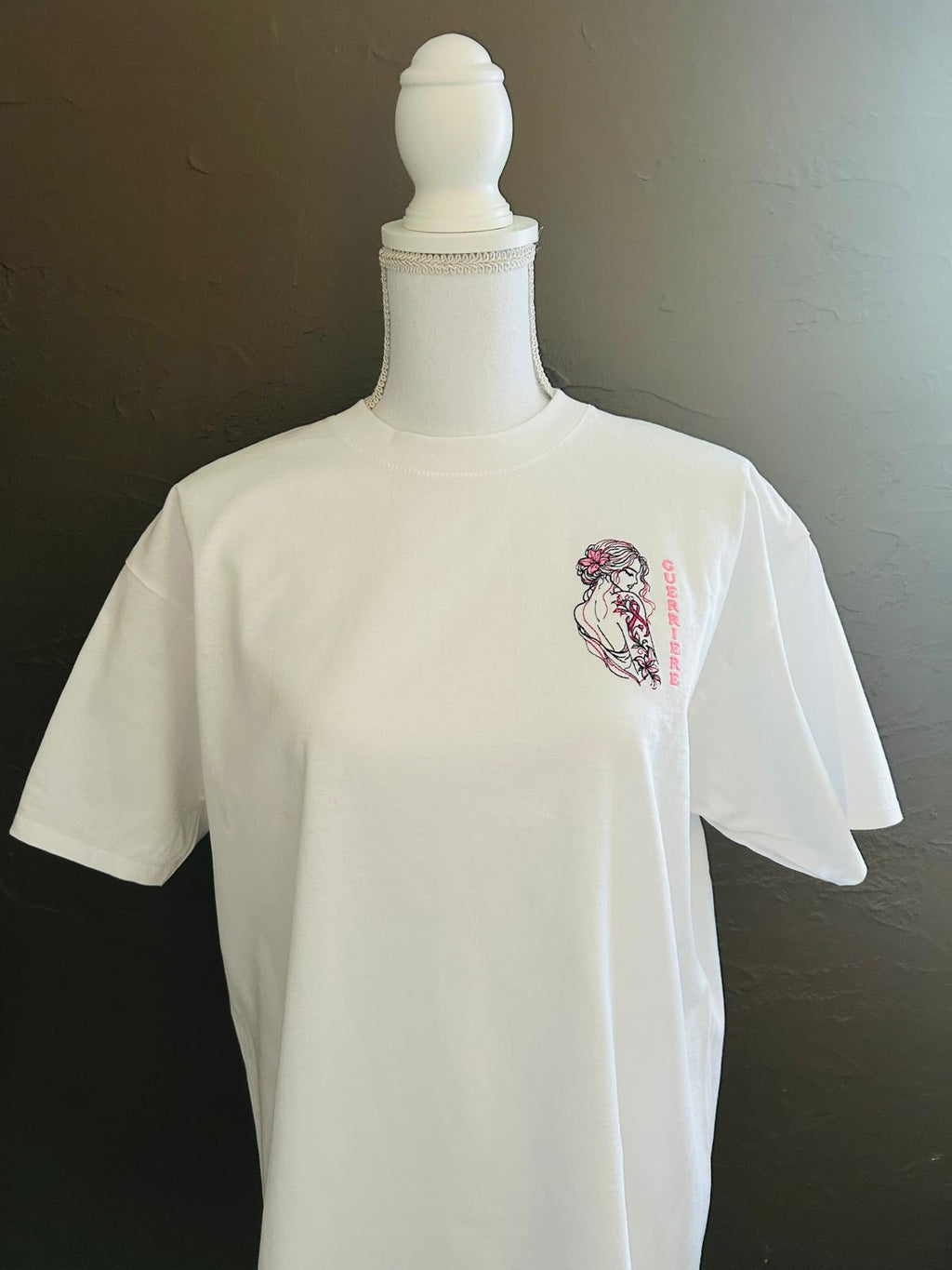 T-shirt blanc coupe classique brodé avec le motif Guerrière Octobre Rose, création originale AK Broderie avec silhouette féminine, tatouage floral et ruban rose.